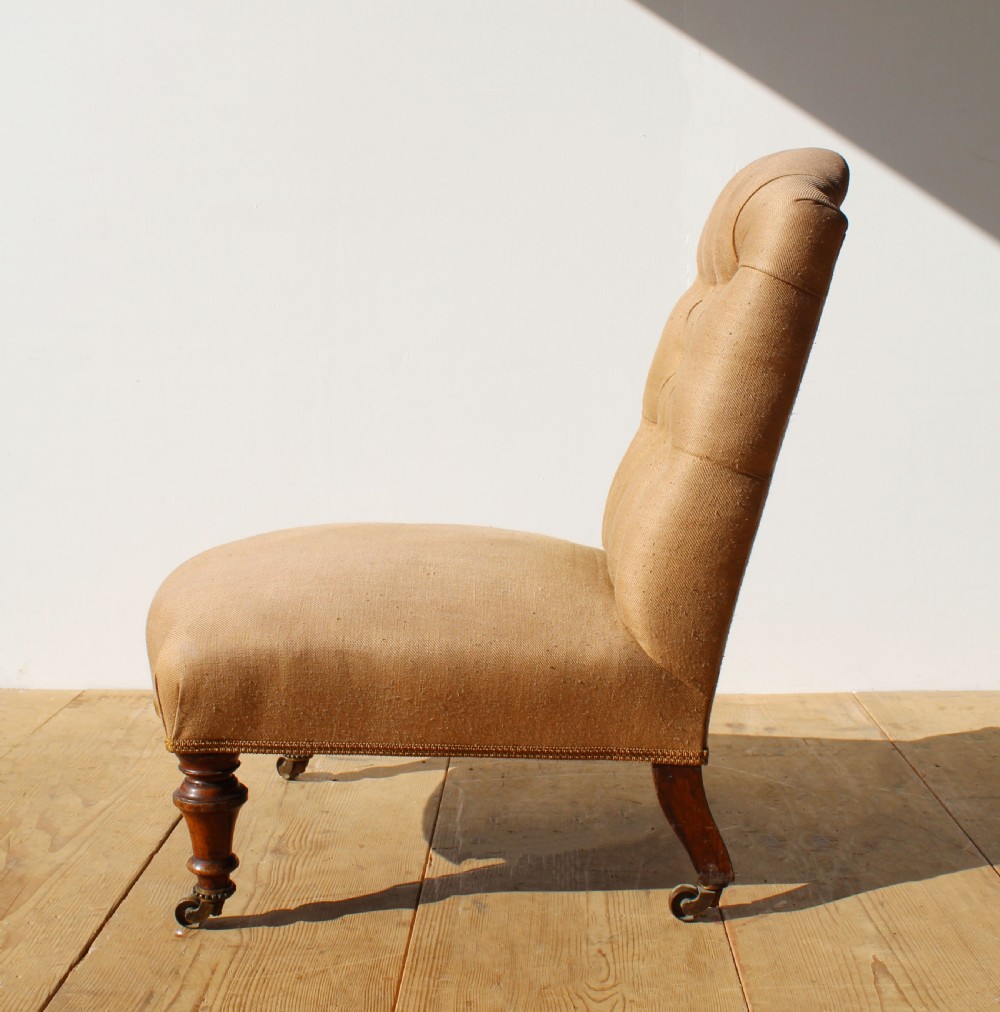 A 19th-century button-back slipper chair upholstered in beige fabric with turned wooden front legs on brass castors.