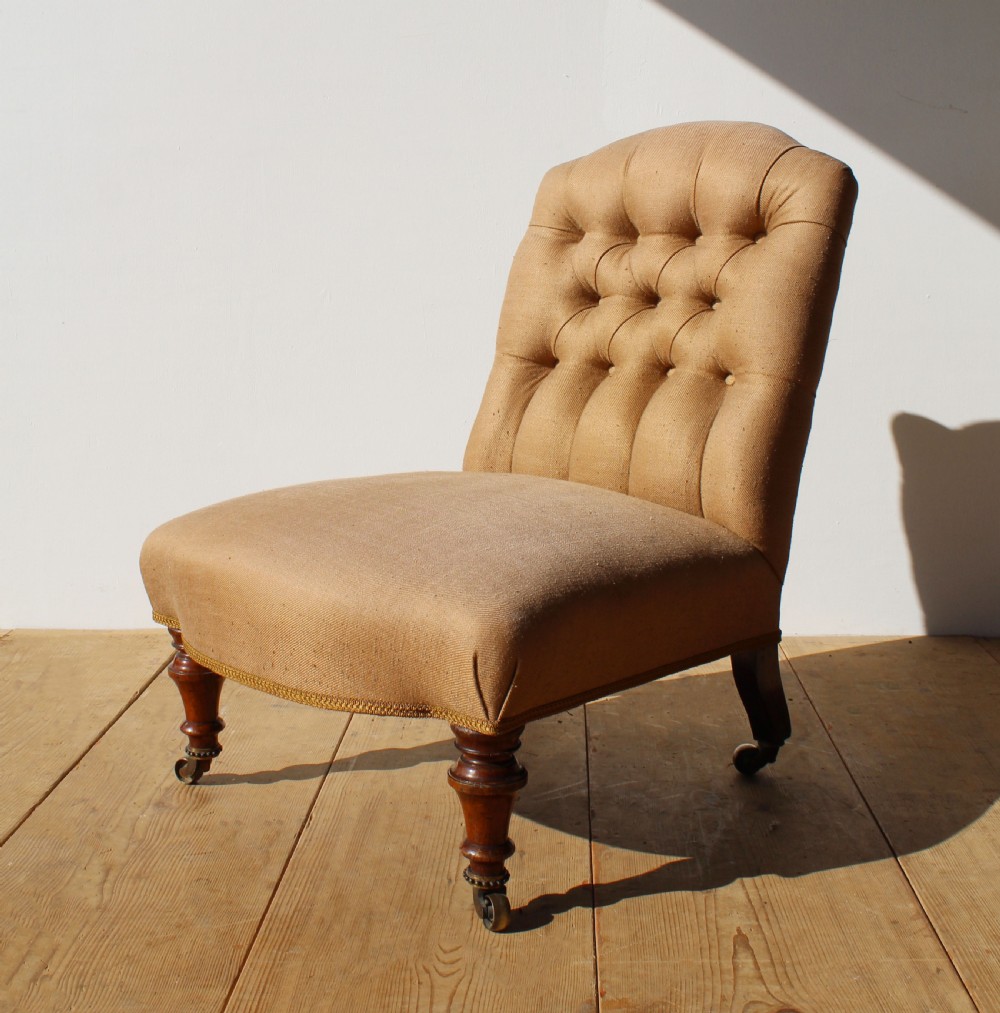 A 19th-century button-back slipper chair upholstered in beige fabric with turned wooden front legs on brass castors. View II