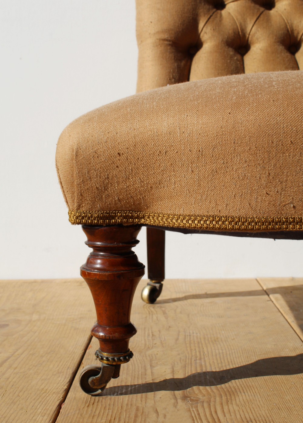 A 19th-century button-back slipper chair upholstered in beige fabric with turned wooden front legs on brass castors. View III