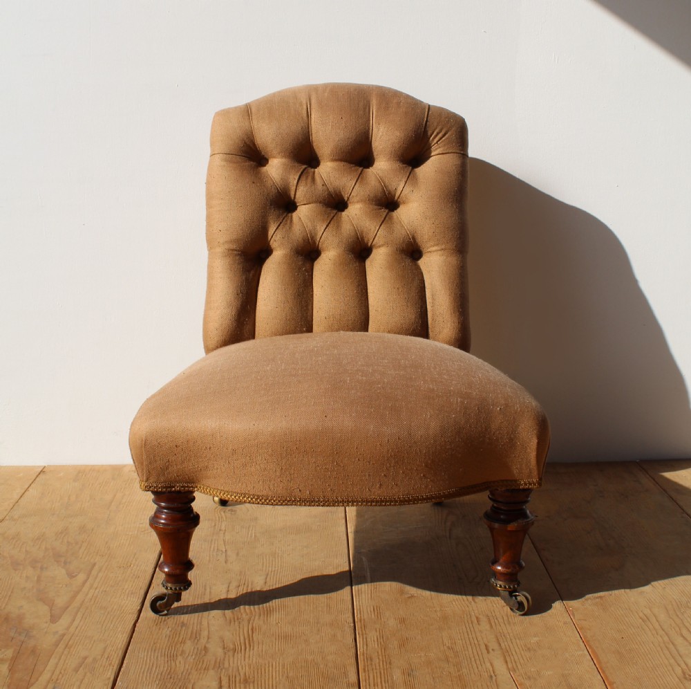 A 19th-century button-back slipper chair upholstered in beige fabric with turned wooden front legs on brass castors. View IV