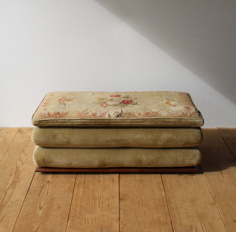 A large 19th-century tiered country ottoman with gold-green velvet upholstery, floral needlepoint top, and a wooden plinth base.