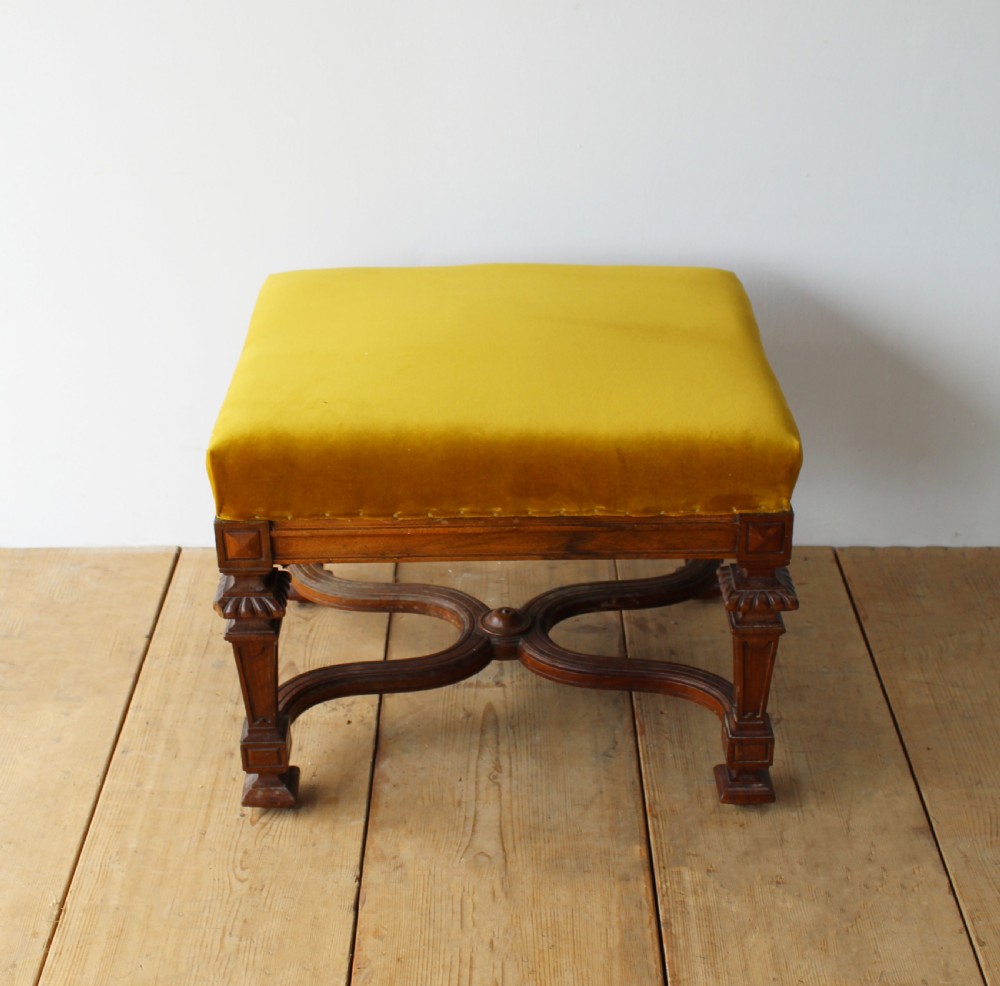 A pair of square upholstered stools featuring mustard yellow velvet seats and carved dark wood legs connected by curved cross-stretchers. View II