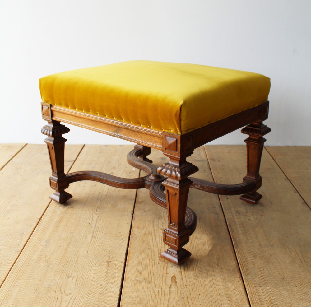 A pair of square upholstered stools featuring mustard yellow velvet seats and carved dark wood legs connected by curved cross-stretchers. View IV