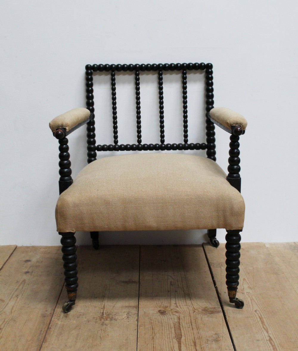 A Victorian ebonised bobbin-turned armchair featuring beige woven fabric upholstery and brass castors.