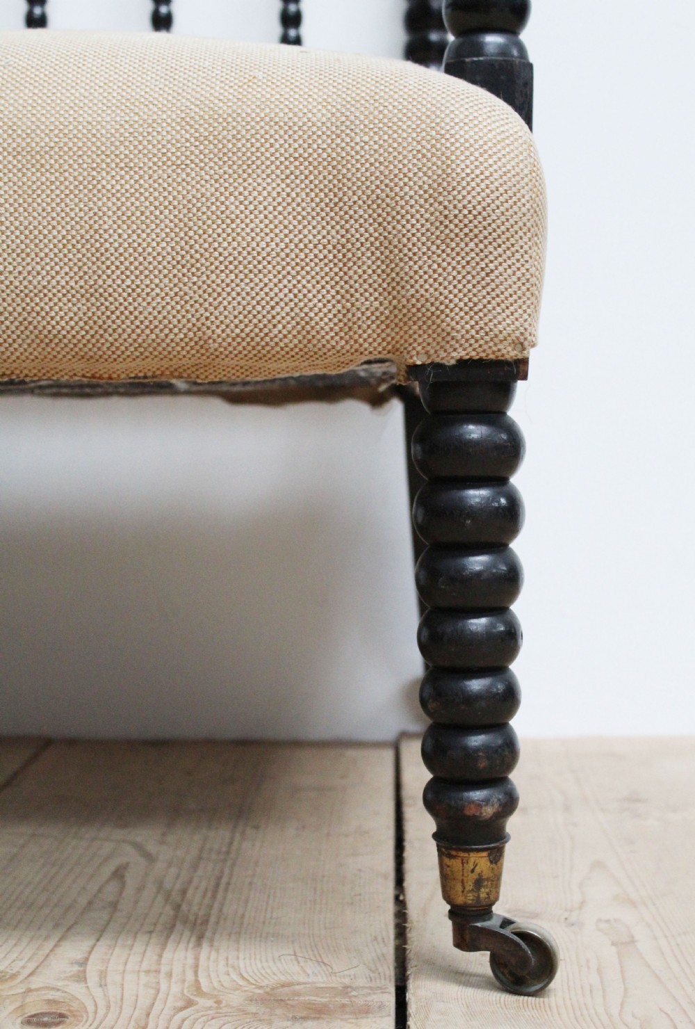 A Victorian ebonised bobbin-turned armchair featuring beige woven fabric upholstery and brass castors. View II