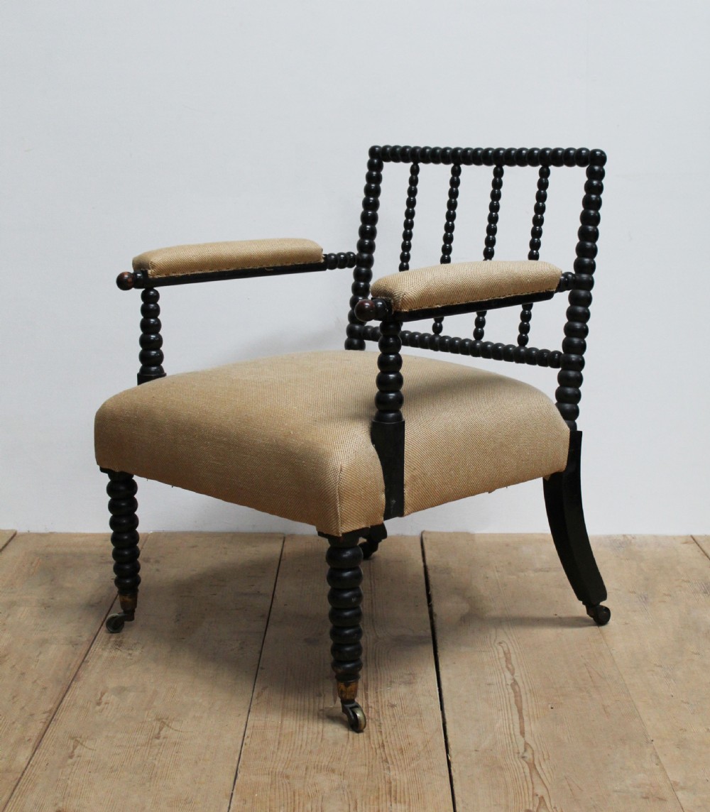 A Victorian ebonised bobbin-turned armchair featuring beige woven fabric upholstery and brass castors. View III