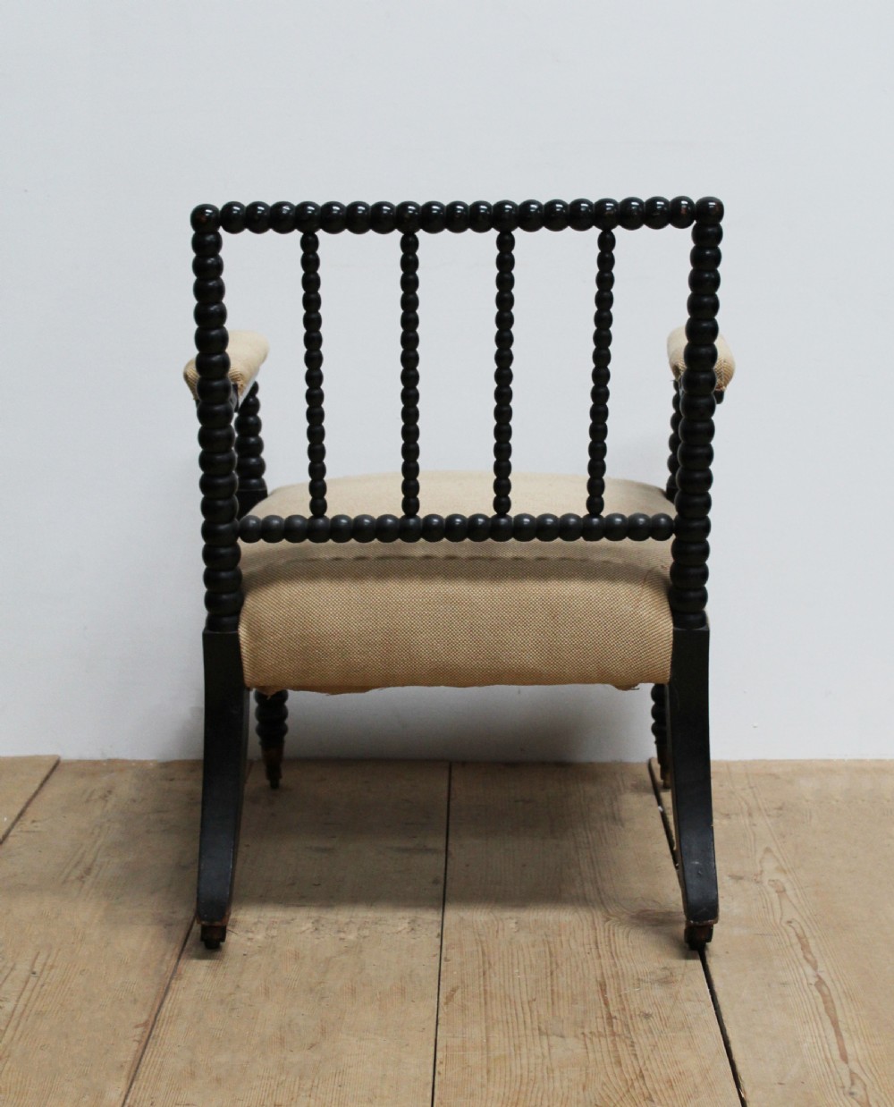A Victorian ebonised bobbin-turned armchair featuring beige woven fabric upholstery and brass castors. View IV