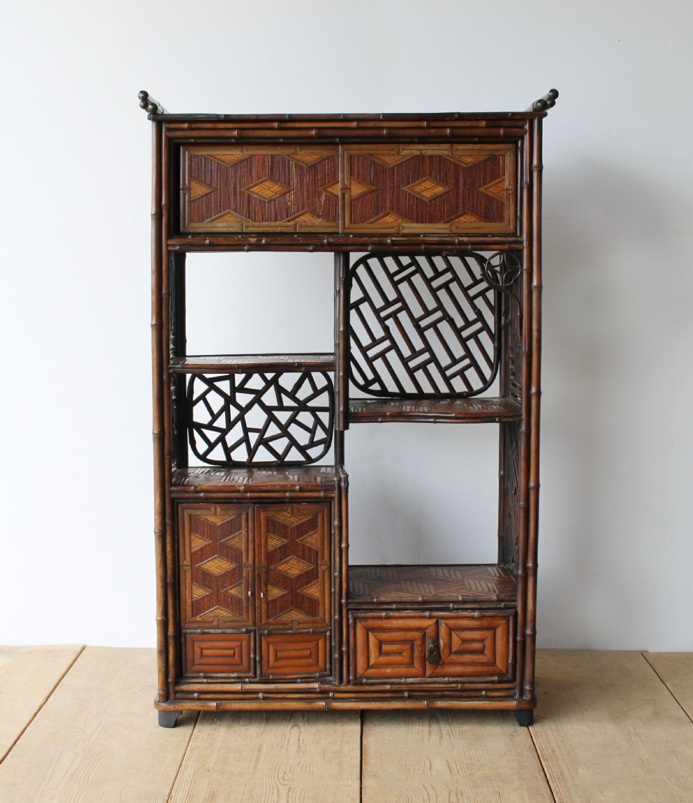 A late 19th-century Victorian bamboo display cabinet featuring asymmetrical shelving, geometric straw parquetry cupboard doors, and decorative lattice back panels.
