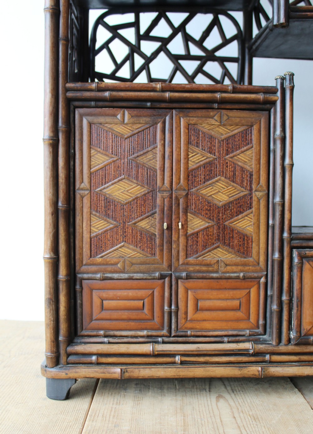 A late 19th-century Victorian bamboo display cabinet featuring asymmetrical shelving, geometric straw parquetry cupboard doors, and decorative lattice back panels. View II