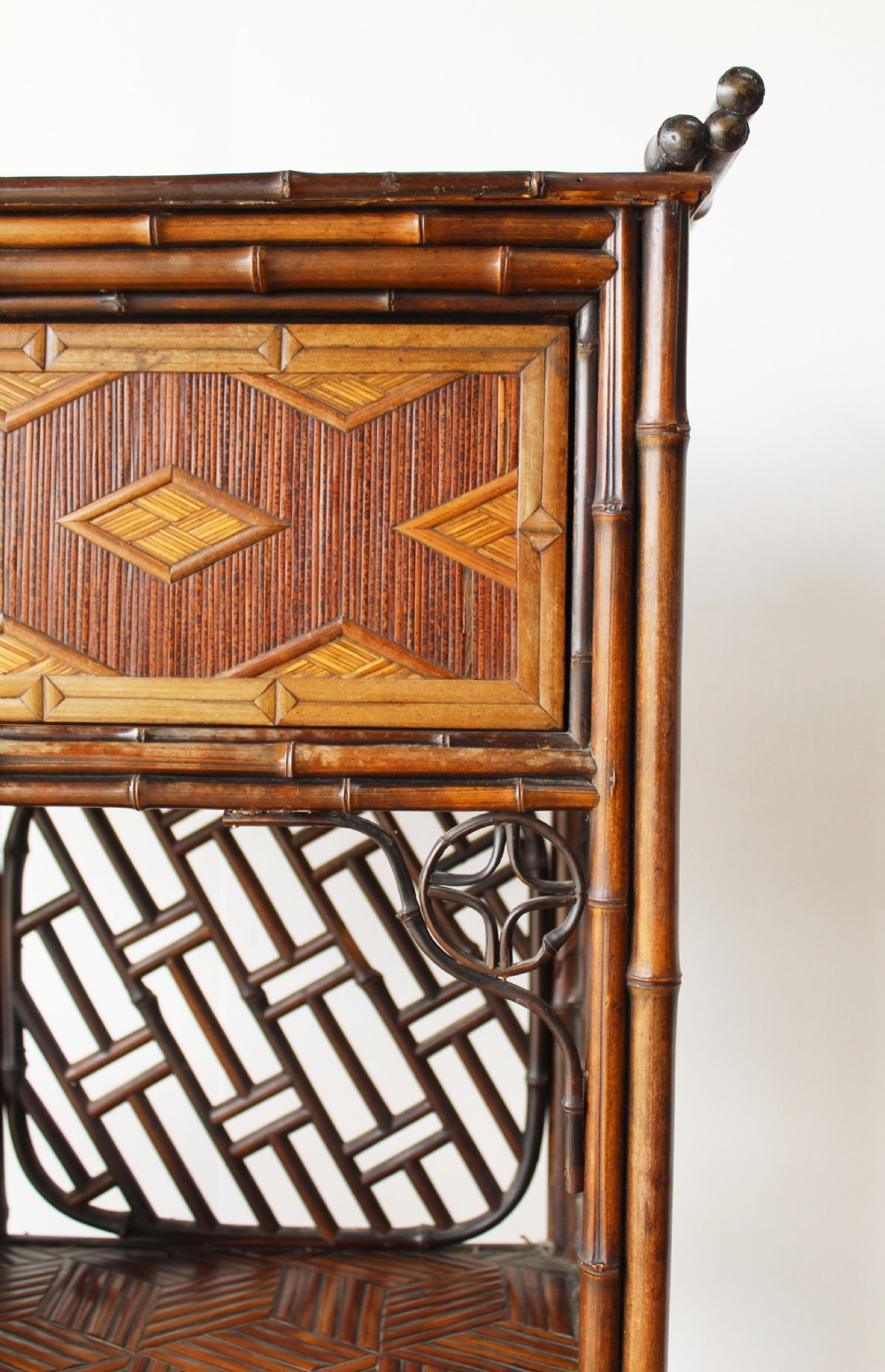 A late 19th-century Victorian bamboo display cabinet featuring asymmetrical shelving, geometric straw parquetry cupboard doors, and decorative lattice back panels. View III