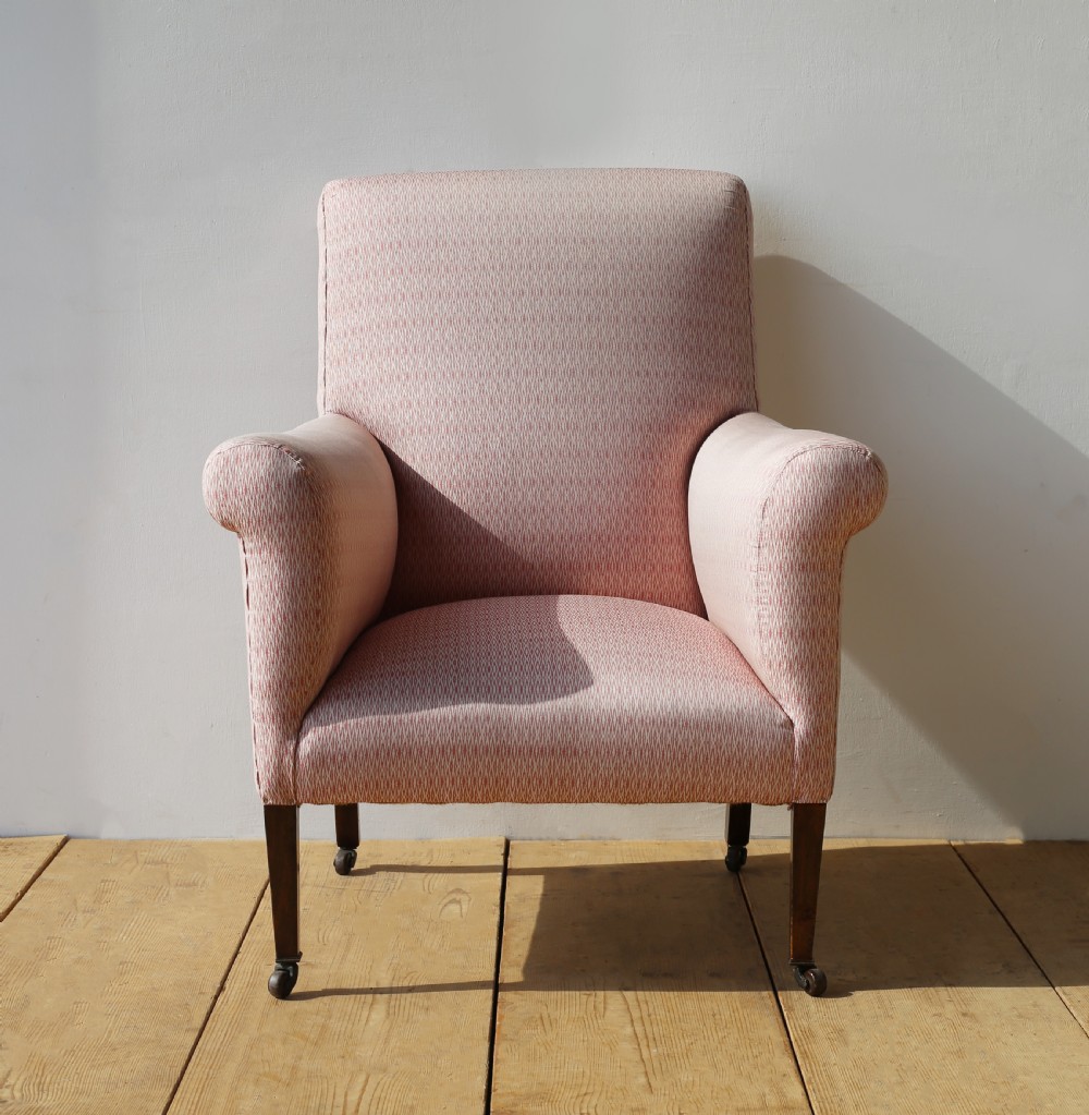 A 19th-century upholstered armchair featuring dusky pink patterned fabric, scrolled arms, square tapered front legs, and brass castors.