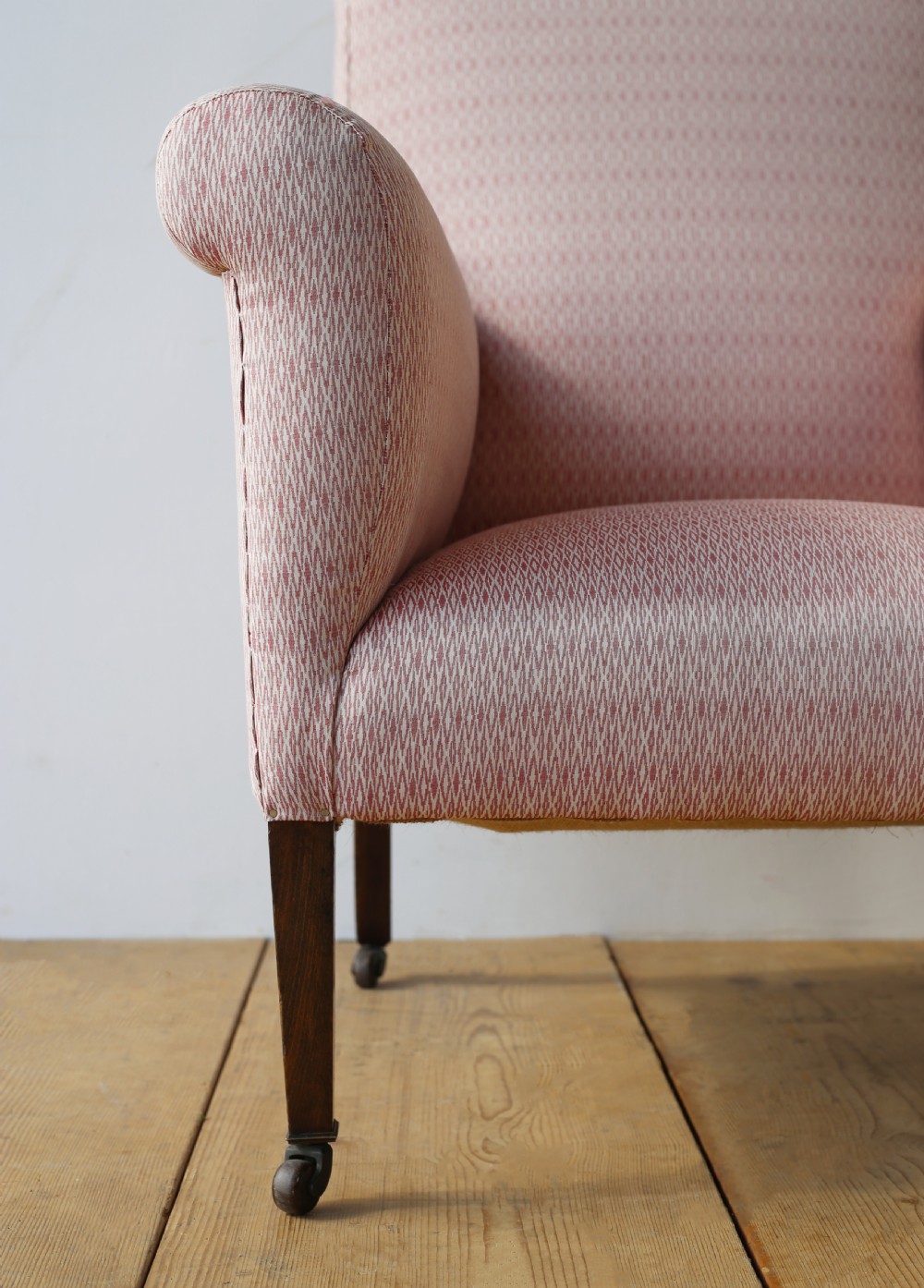 A 19th-century upholstered armchair featuring dusky pink patterned fabric, scrolled arms, square tapered front legs, and brass castors. View II