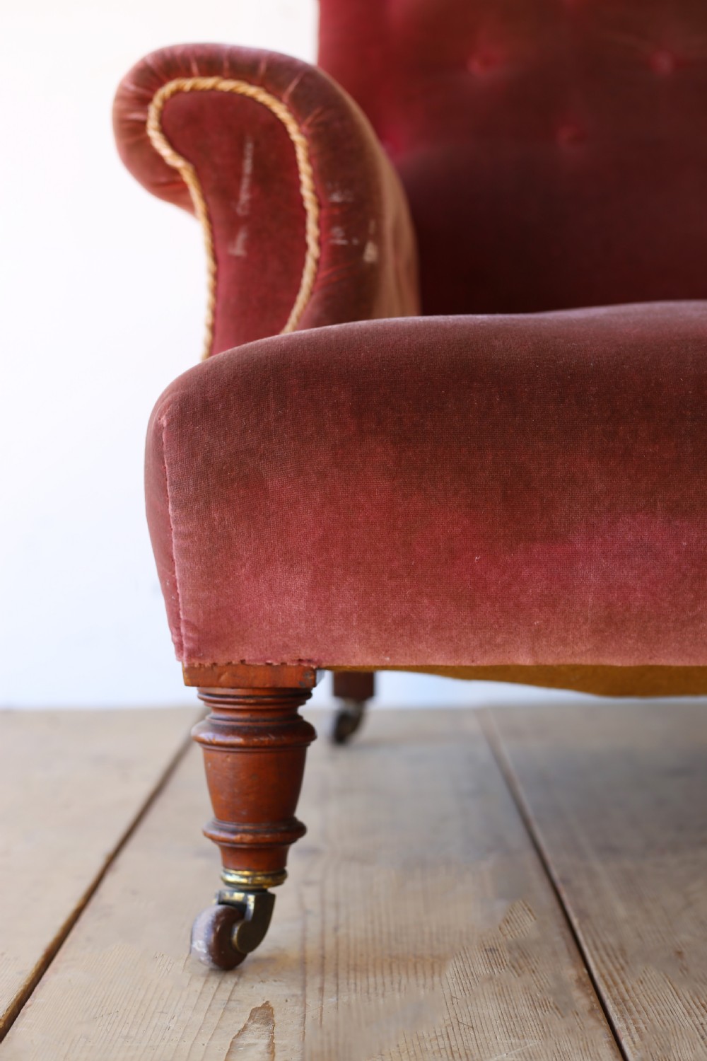 A 19th-century Victorian armchair upholstered in deep red velvet, featuring a buttoned backrest, scrolled arms with braid trim, and turned wooden front legs on brass castors. View II