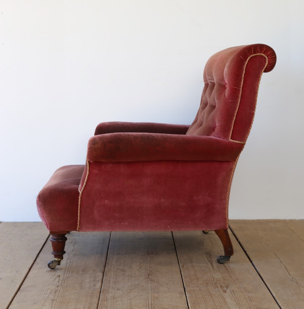 A 19th-century Victorian armchair upholstered in deep red velvet, featuring a buttoned backrest, scrolled arms with braid trim, and turned wooden front legs on brass castors. View IV