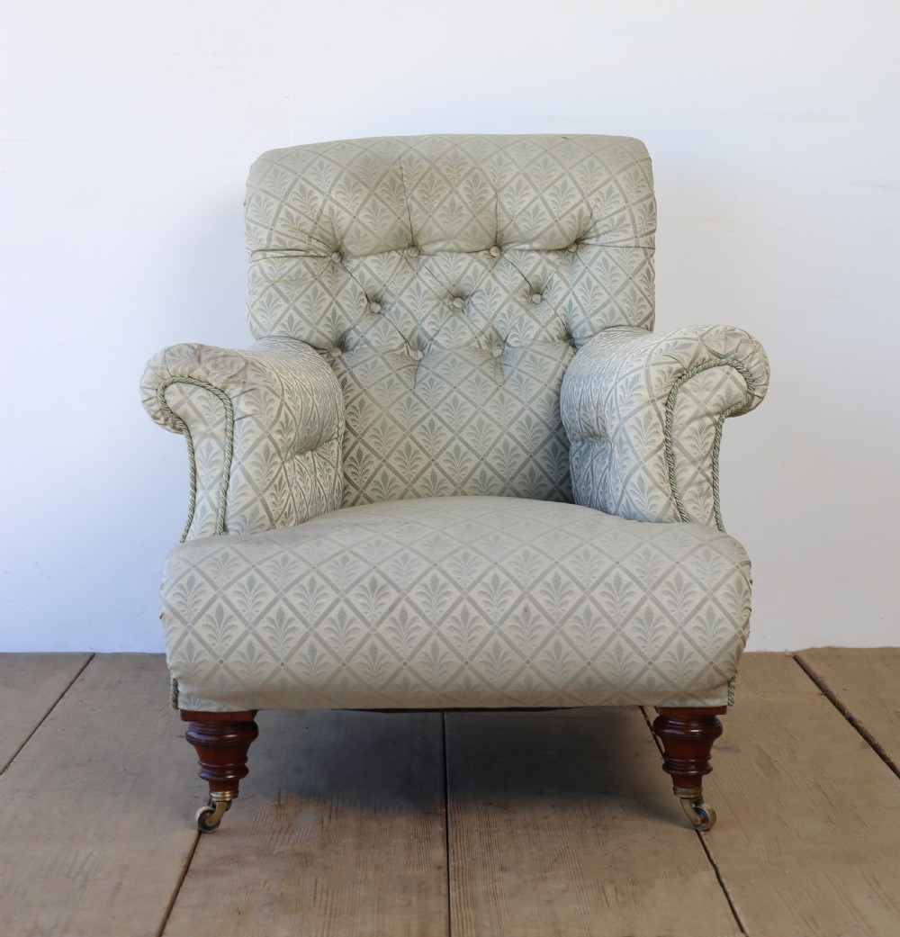 A Victorian button-backed armchair upholstered in sage green patterned fabric with scrolled arms, turned mahogany front legs, and brass castors.