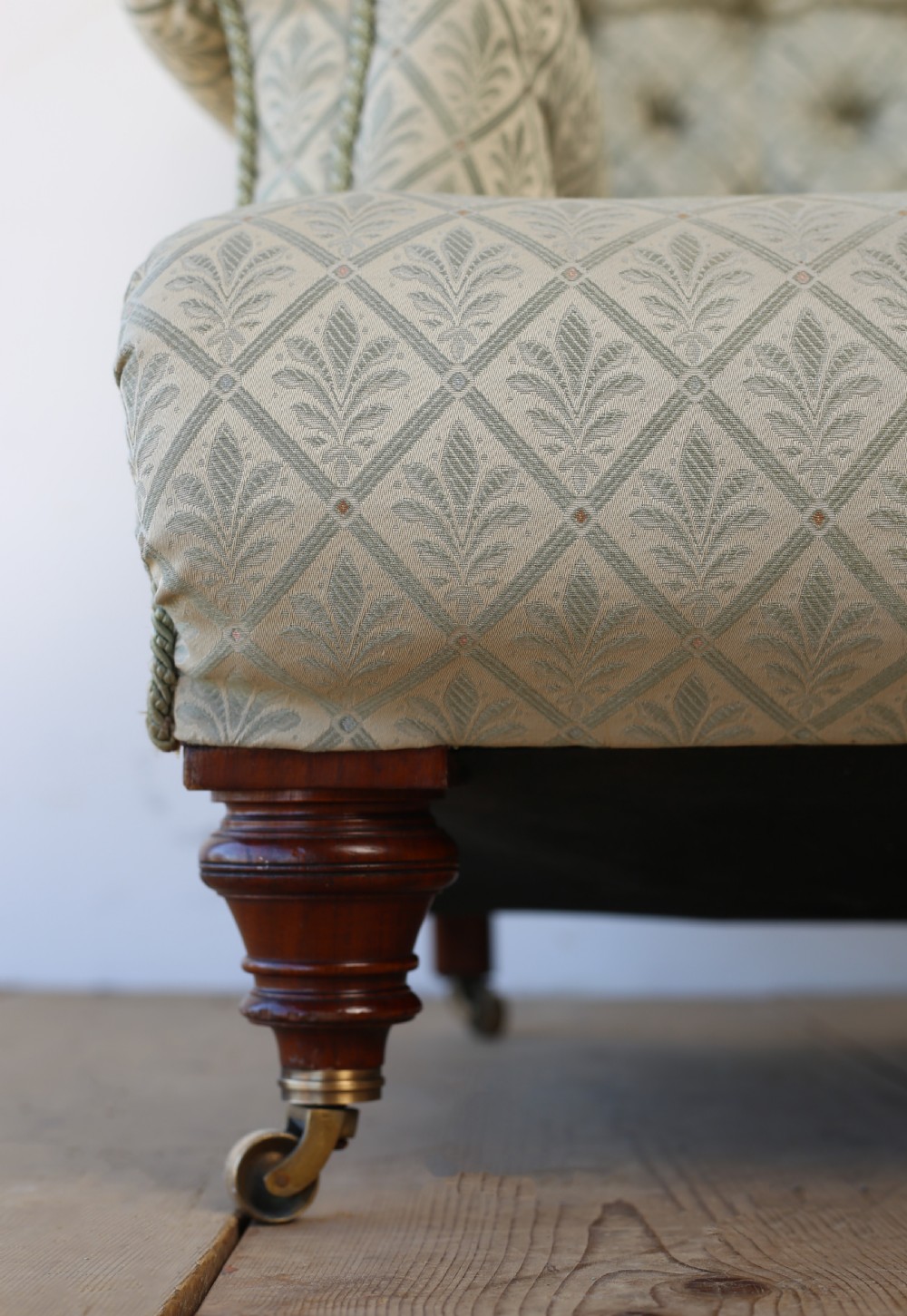 A Victorian button-backed armchair upholstered in sage green patterned fabric with scrolled arms, turned mahogany front legs, and brass castors. View II