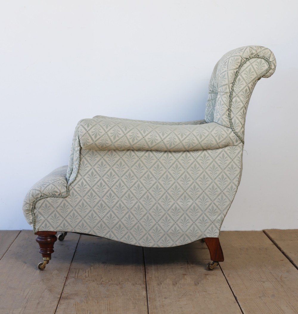 A Victorian button-backed armchair upholstered in sage green patterned fabric with scrolled arms, turned mahogany front legs, and brass castors. View V