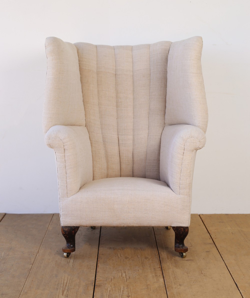 A high-backed 19th-century barrel back armchair with vertical fluting, upholstered in neutral off-white fabric on turned timber legs with brass castors.