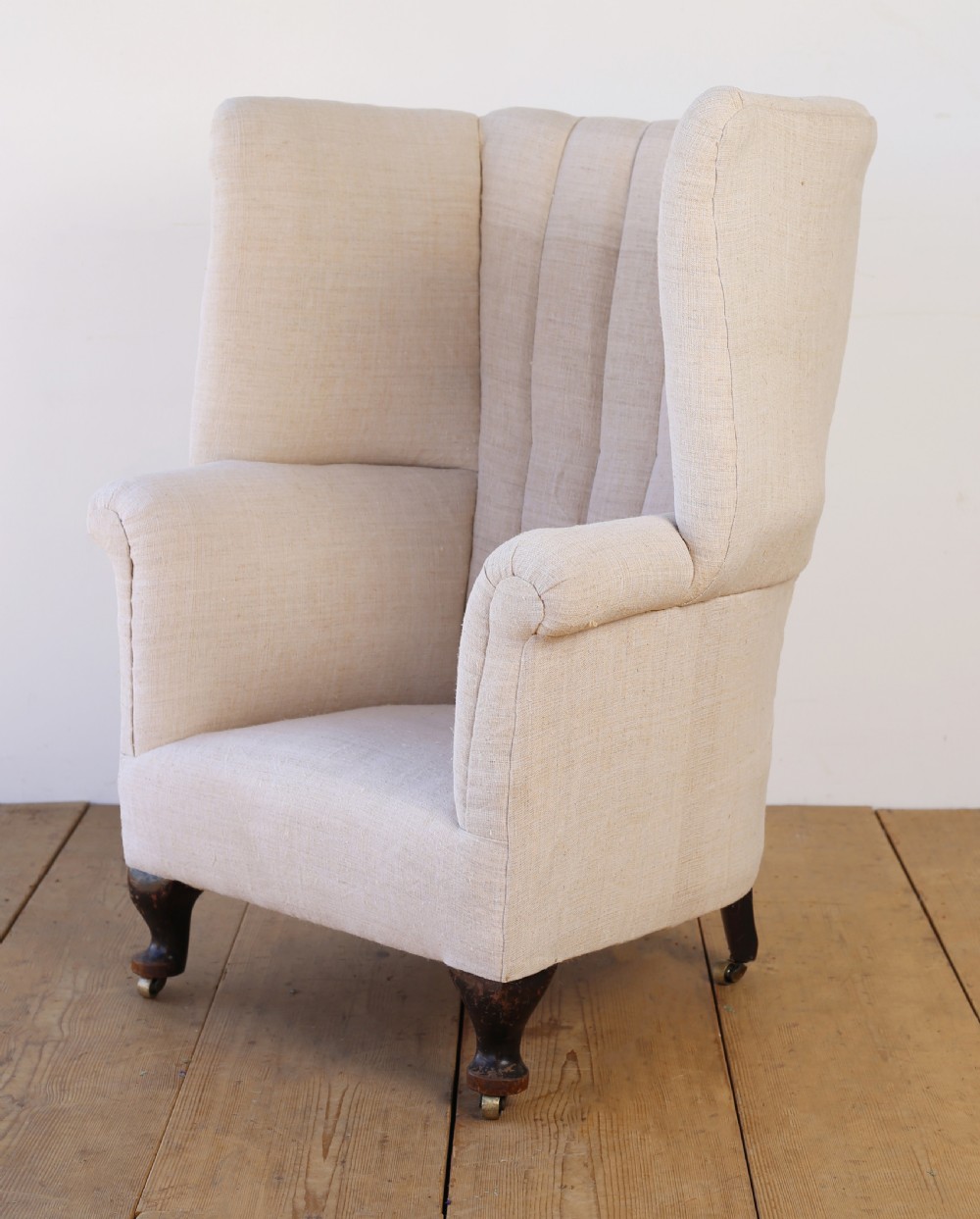 A high-backed 19th-century barrel back armchair with vertical fluting, upholstered in neutral off-white fabric on turned timber legs with brass castors. View III
