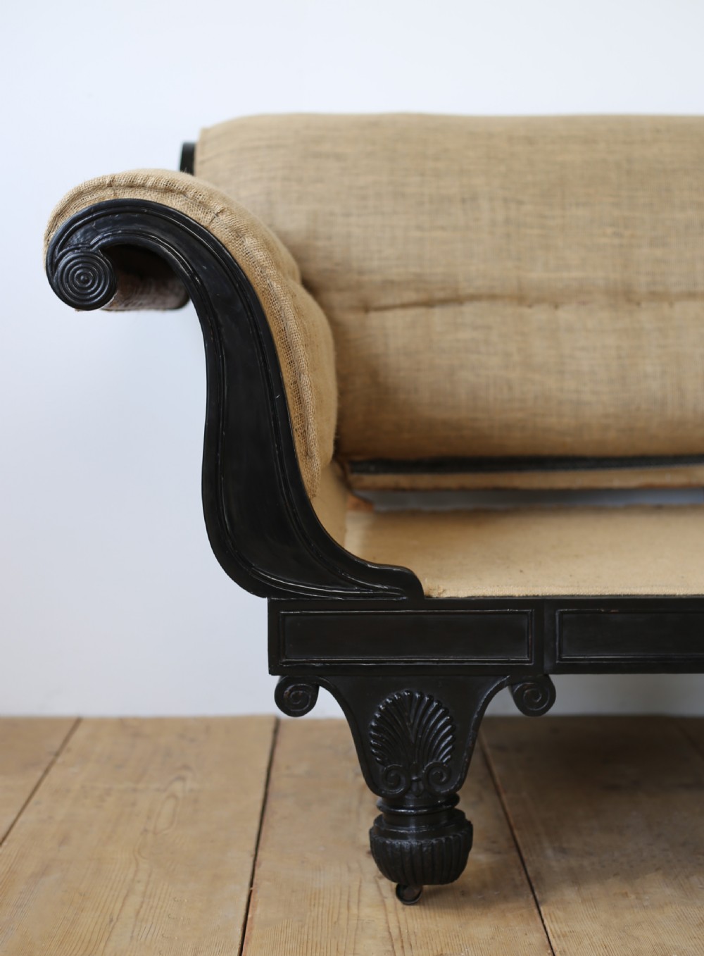 A 19th-century Regency sofa featuring an ebonised dark wooden frame with scrolled arms, carved feet, and natural hessian lining. View II