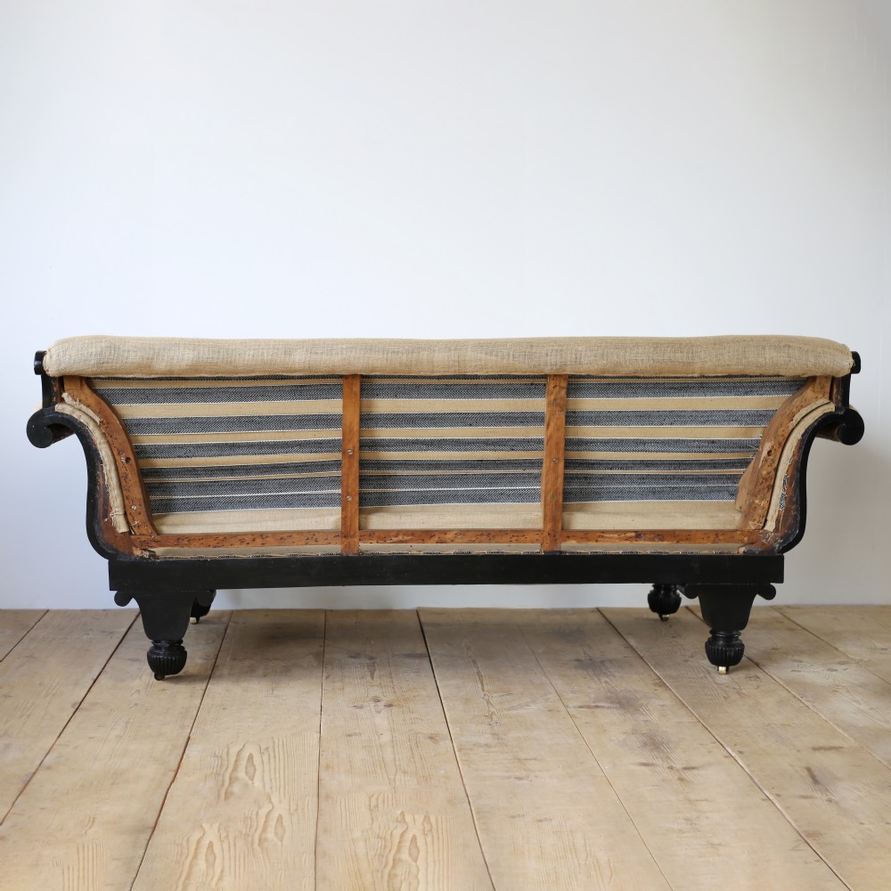 A 19th-century Regency sofa featuring an ebonised dark wooden frame with scrolled arms, carved feet, and natural hessian lining. View IV