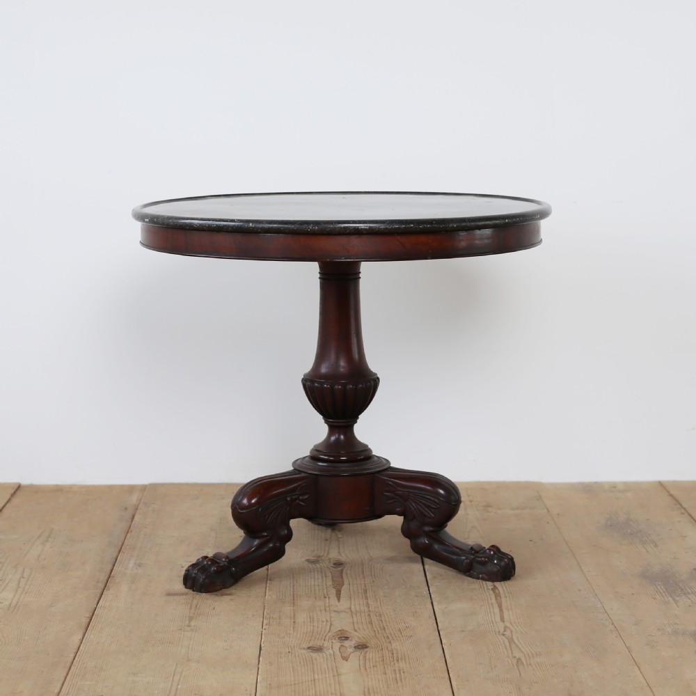 A circular Empire mahogany gueridon table featuring a dark marble top, turned pedestal stem, and carved tripod paw feet.