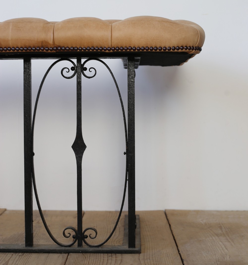 A 1920s English club fender featuring a buttoned tan leather bench top resting on a wrought iron baluster frame with scroll details. View III