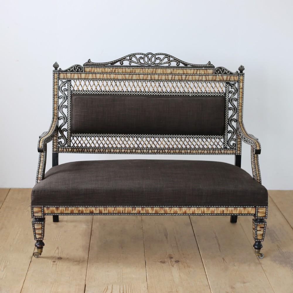 A nineteenth-century Anglo-Indian porcupine quill settee crafted from dark ebony wood with geometric bone dot inlay and dark brown fabric upholstery.