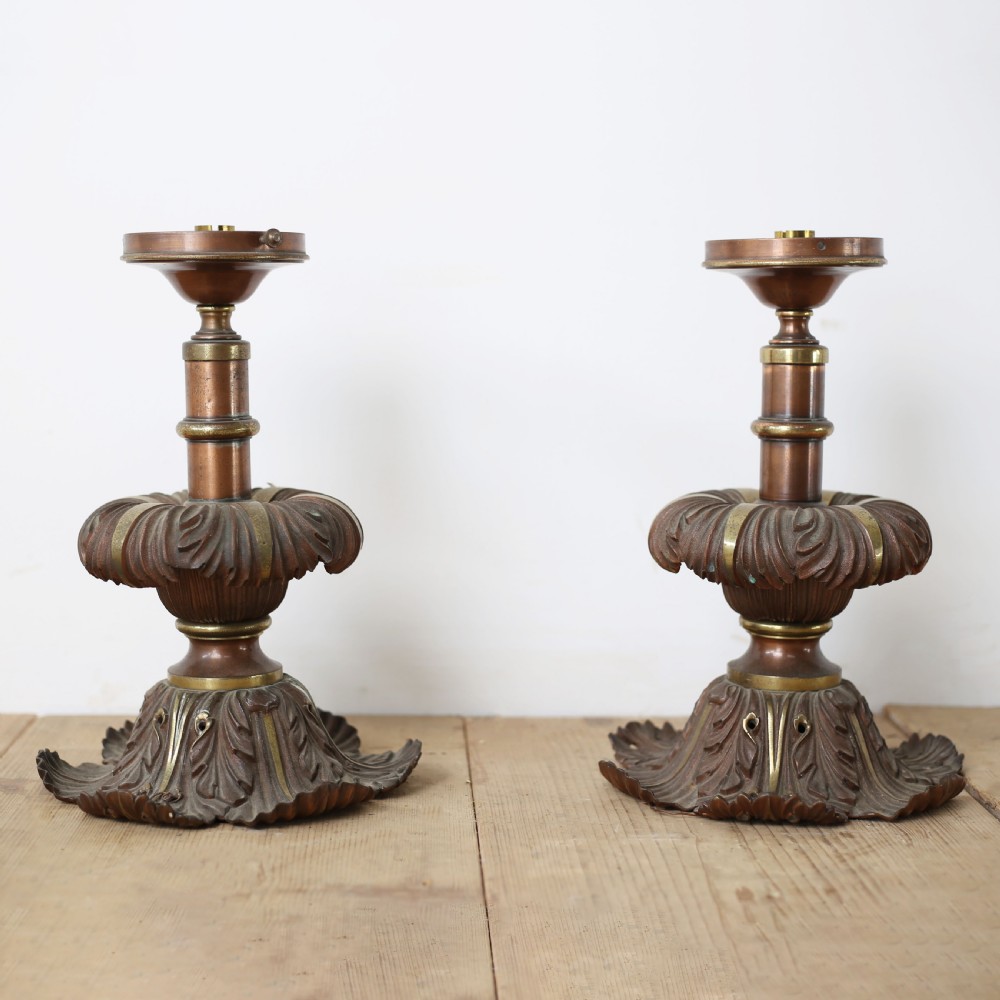 A pair of cast bronze and brass light bases featuring relief-carved acanthus leaf motifs and knopped central stems on a wooden surface.