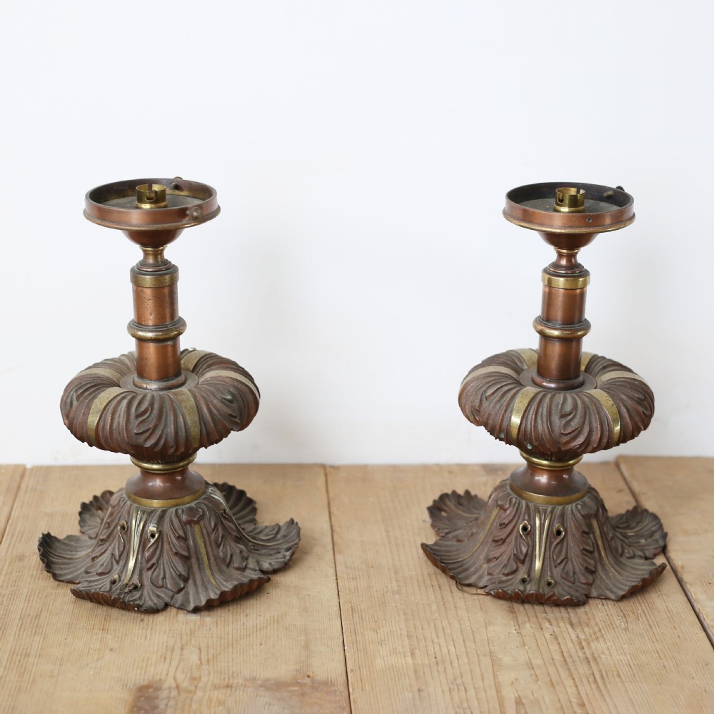 A pair of cast bronze and brass light bases featuring relief-carved acanthus leaf motifs and knopped central stems on a wooden surface. View III