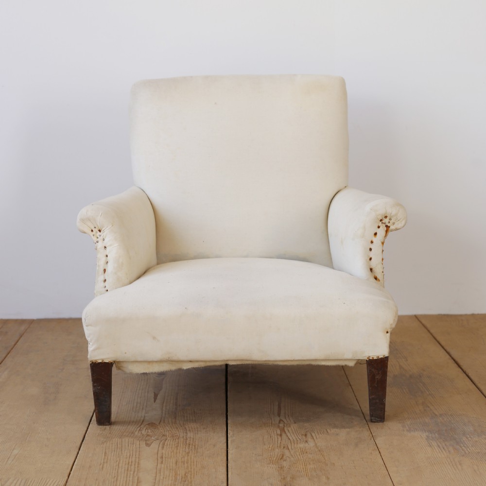 A 19th-century Howard style armchair upholstered in off-white calico fabric with exposed dark wood tapered front legs and brass studding along the scrolled arm fronts.