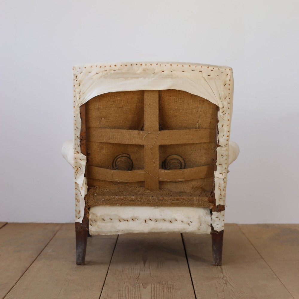 A 19th-century Howard style armchair upholstered in off-white calico fabric with exposed dark wood tapered front legs and brass studding along the scrolled arm fronts. View V