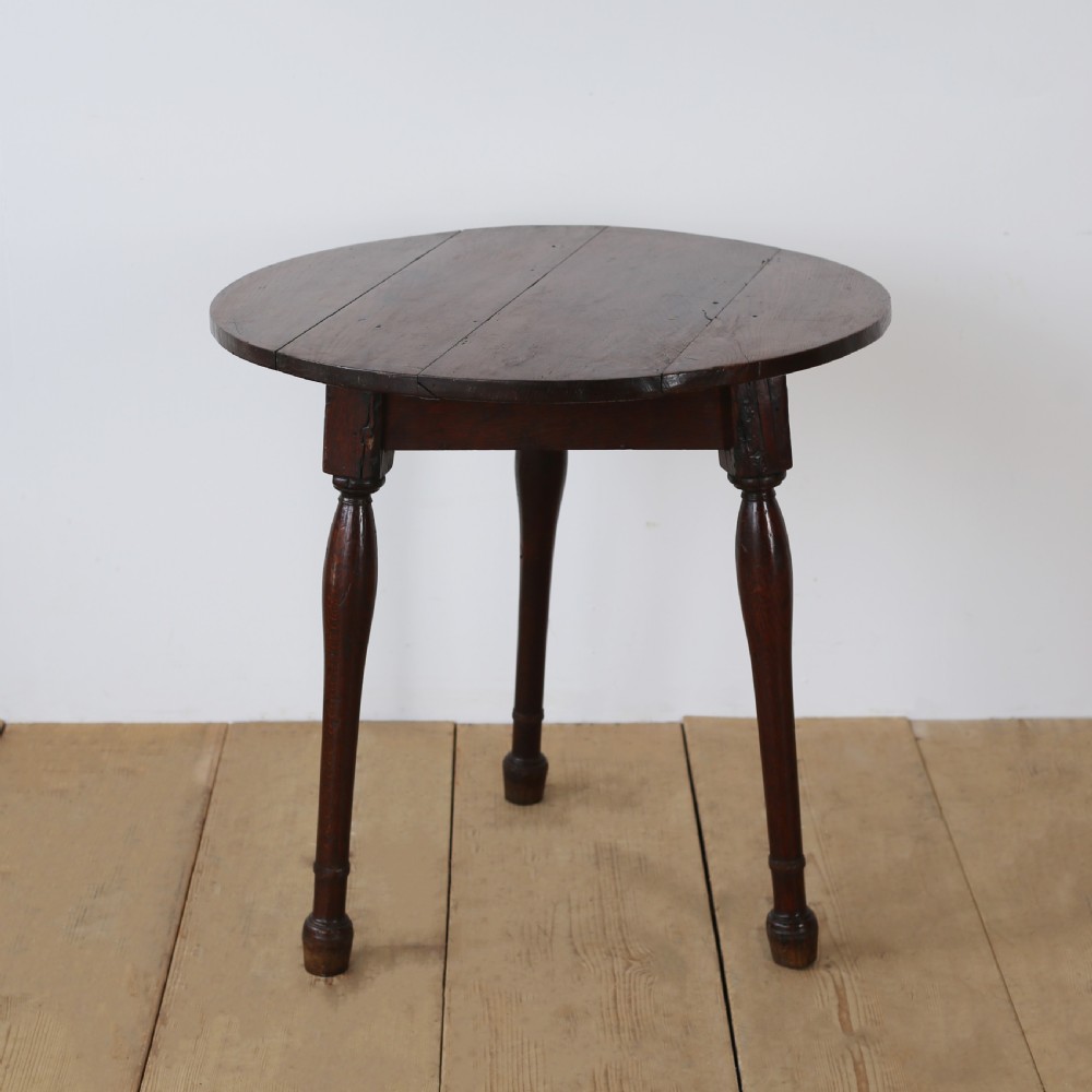 A dark oak 17th-century cricket table featuring a circular plank top and three turned legs.