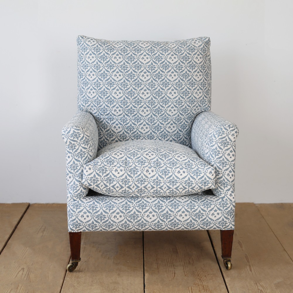 A Victorian upholstered armchair featuring a blue and white printed fabric, turned wooden front legs, and brass castors.
