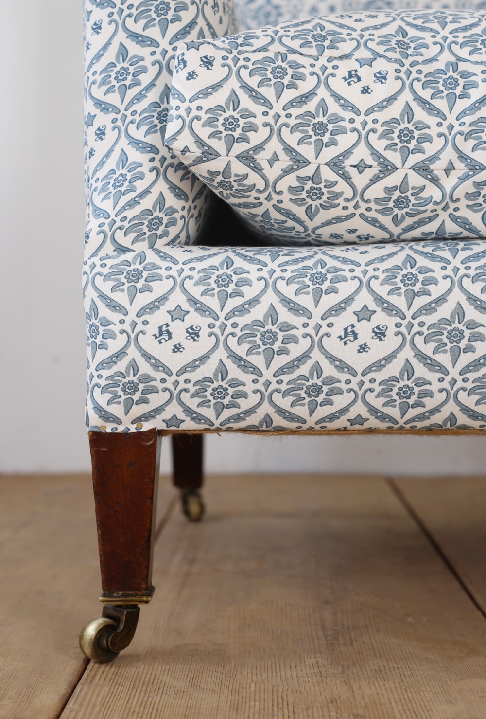 A Victorian upholstered armchair featuring a blue and white printed fabric, turned wooden front legs, and brass castors. View II