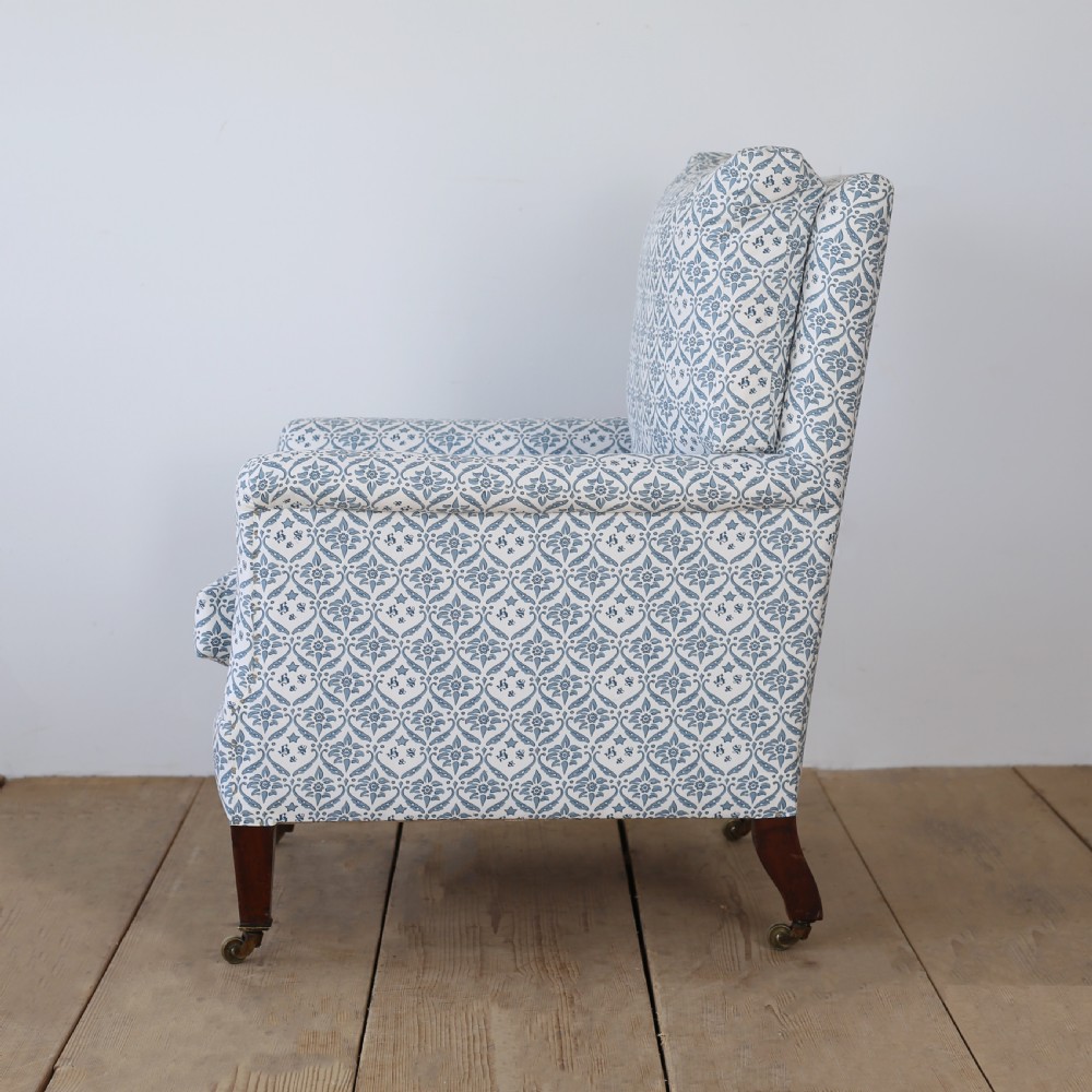 A Victorian upholstered armchair featuring a blue and white printed fabric, turned wooden front legs, and brass castors. View VI