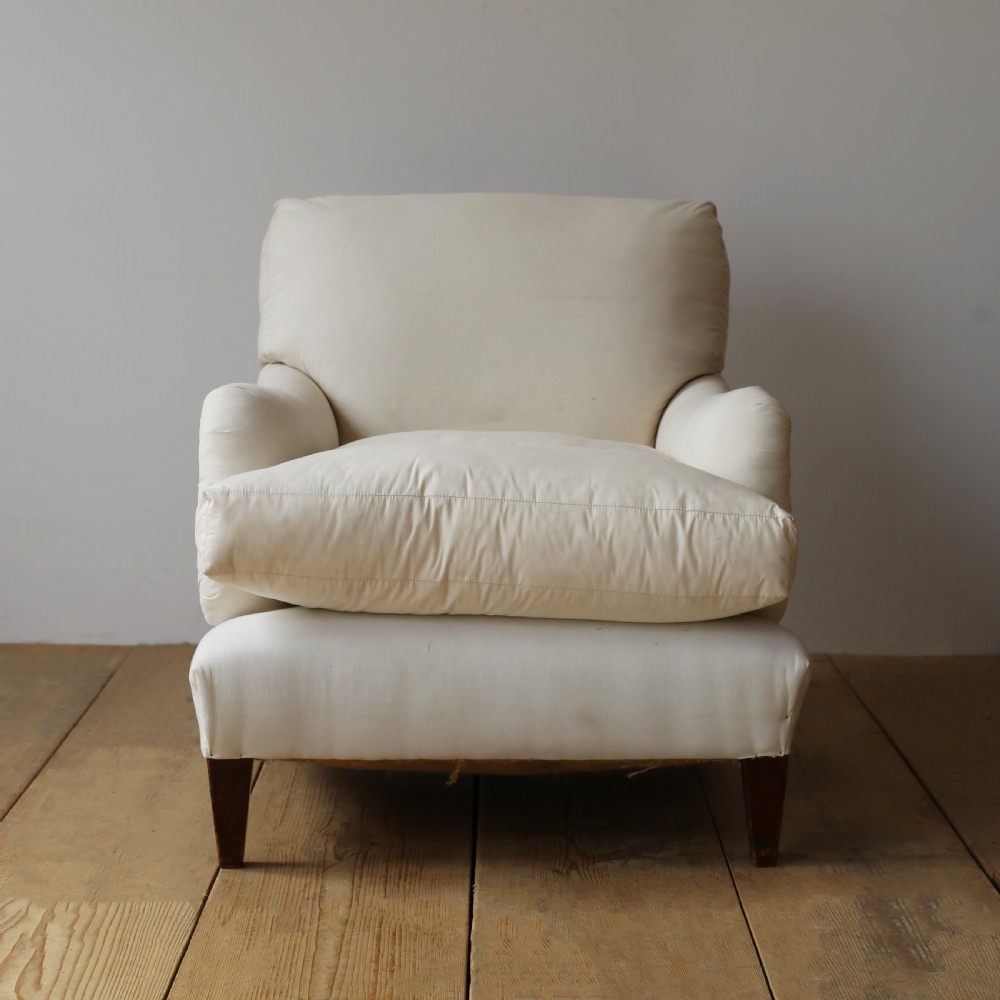 A cream calico upholstered Howard style armchair with a deep feather seat cushion, low rolled arms, and tapered dark wood legs.