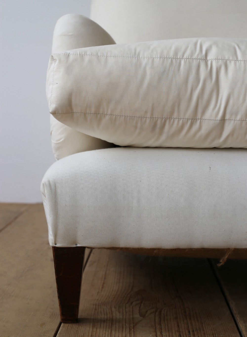 A cream calico upholstered Howard style armchair with a deep feather seat cushion, low rolled arms, and tapered dark wood legs. View II
