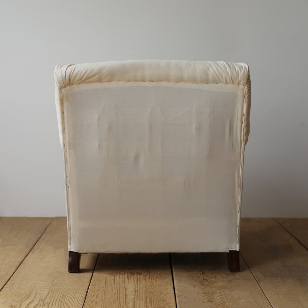 A cream calico upholstered Howard style armchair with a deep feather seat cushion, low rolled arms, and tapered dark wood legs. View V