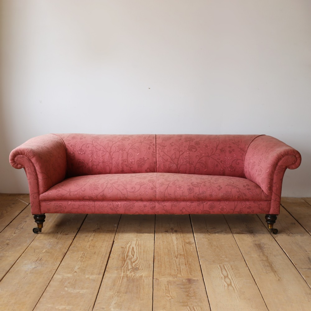 A 19th-century Chesterfield sofa upholstered in rose pink patterned floral fabric, featuring rolled scroll arms and turned wooden legs on brass castors.