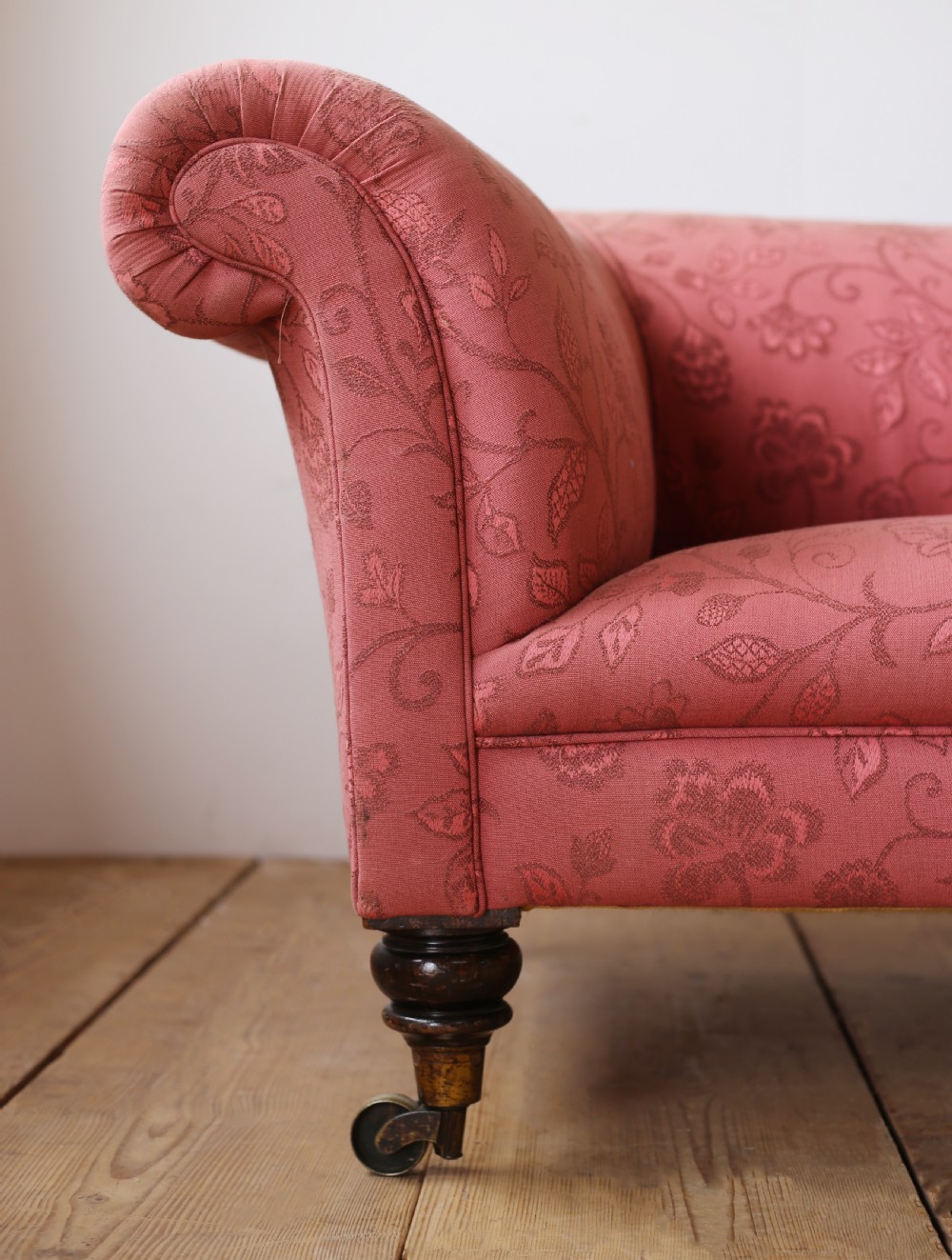 A 19th-century Chesterfield sofa upholstered in rose pink patterned floral fabric, featuring rolled scroll arms and turned wooden legs on brass castors. View II