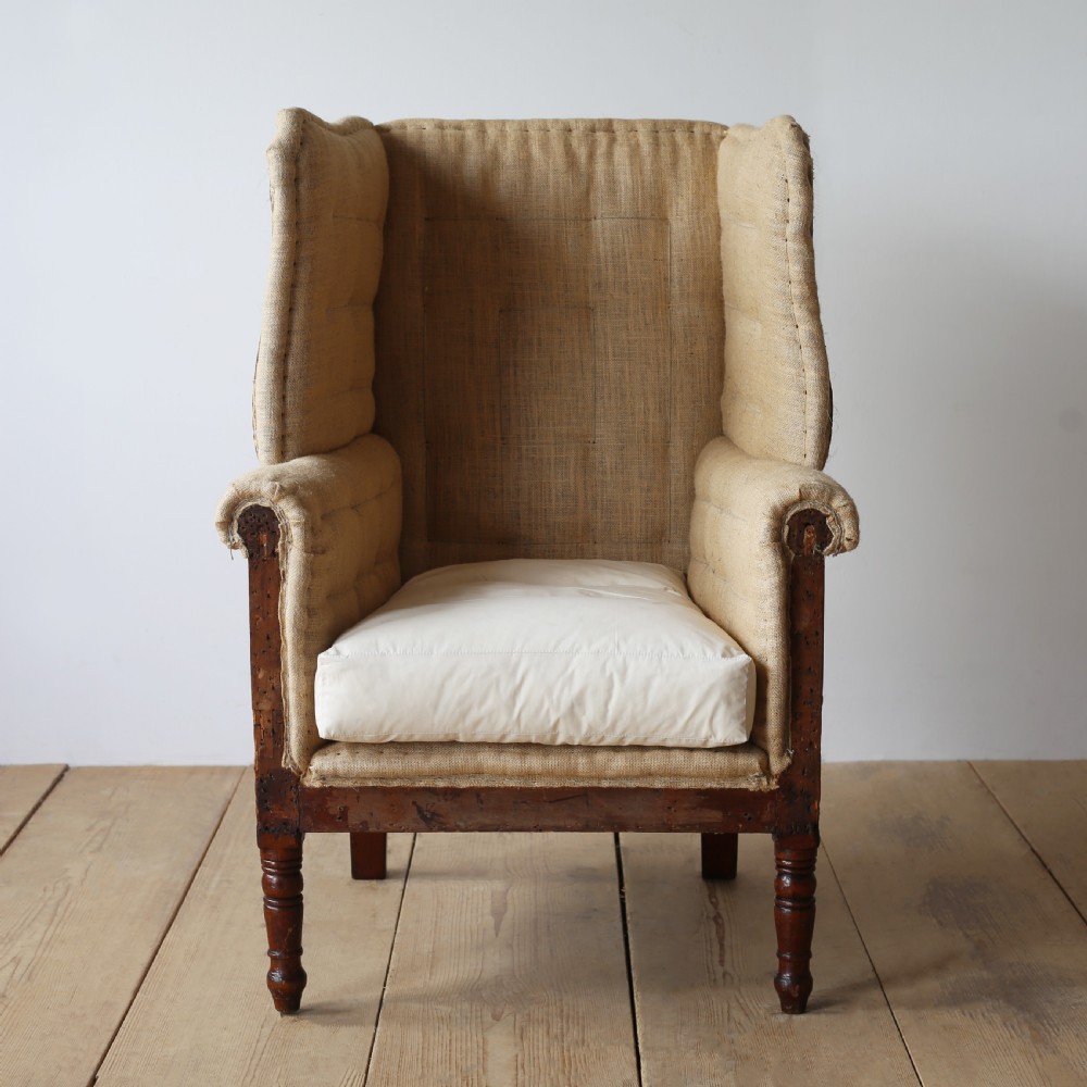 A 19th century wingback armchair presented in hessian upholstery with dark turned front legs and a off-white cushion.