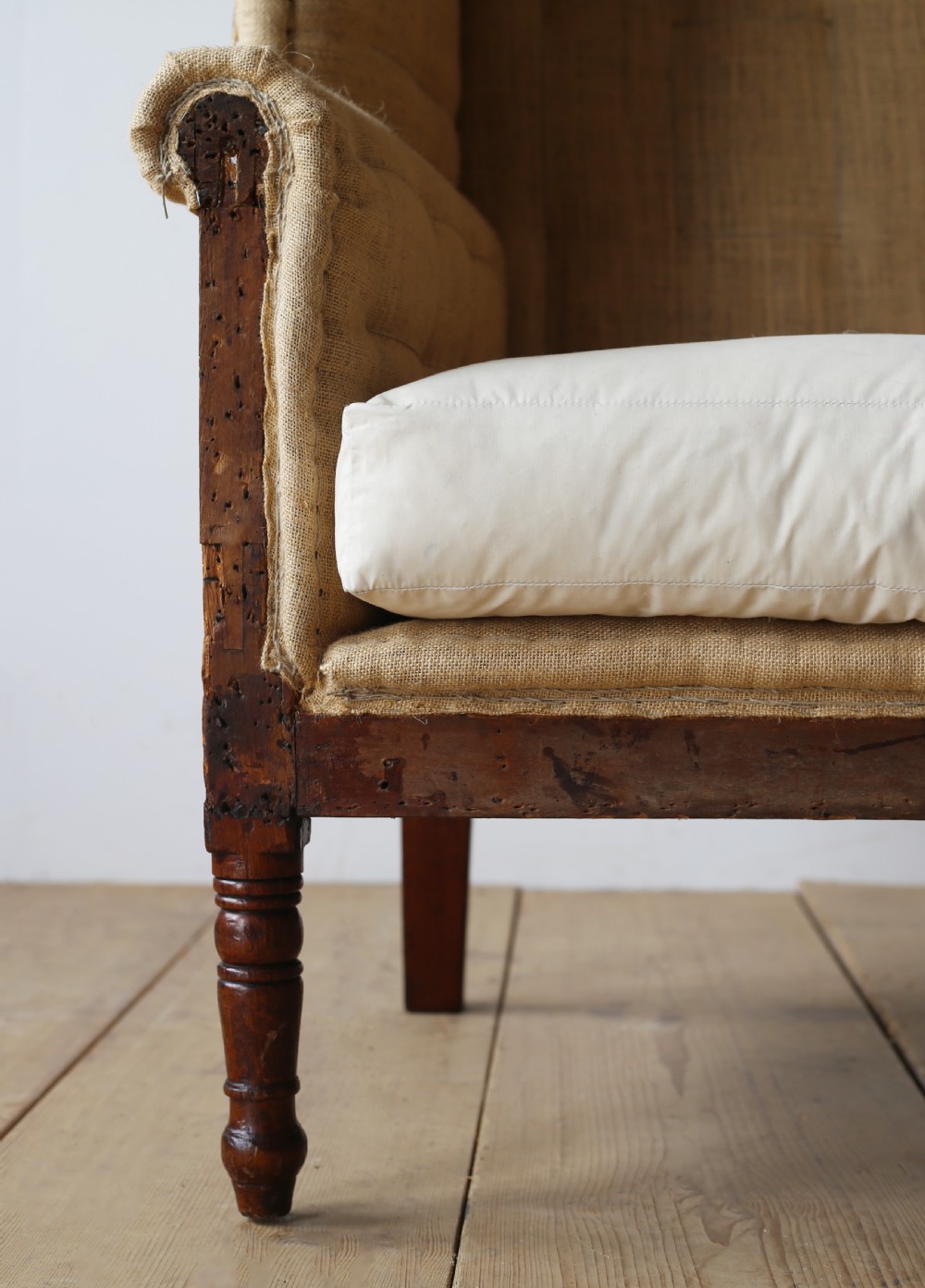 A 19th century wingback armchair presented in hessian upholstery with dark turned front legs and a off-white cushion. View II