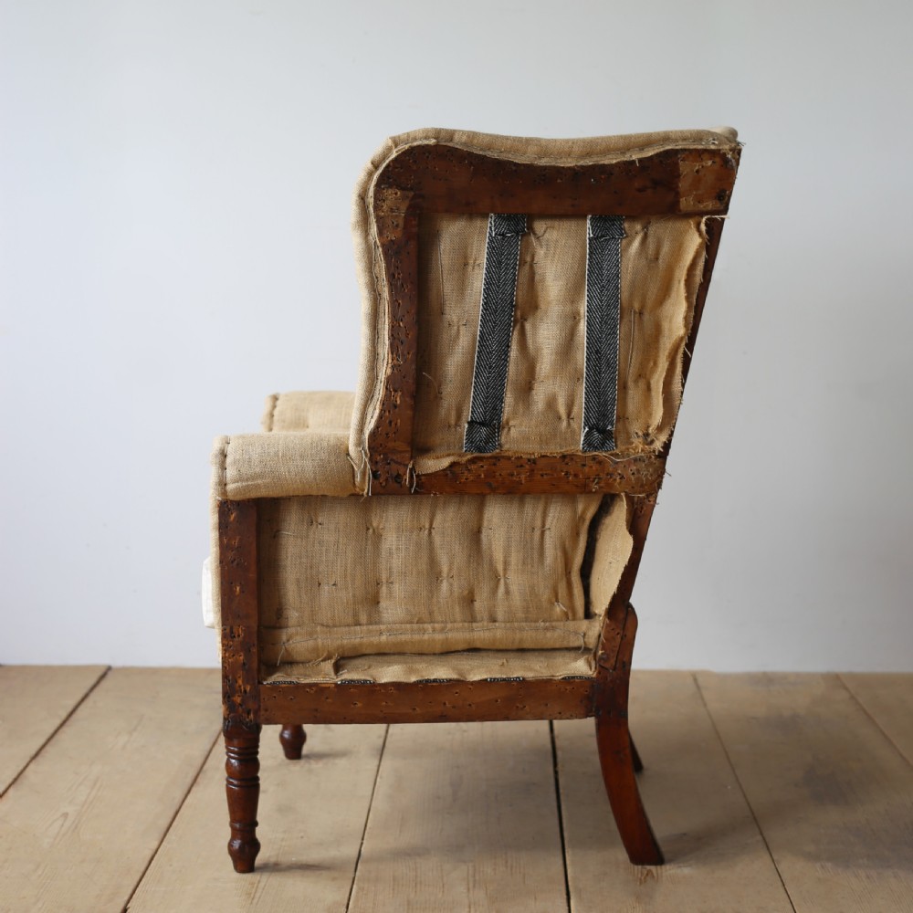 A 19th century wingback armchair presented in hessian upholstery with dark turned front legs and a off-white cushion. View IV
