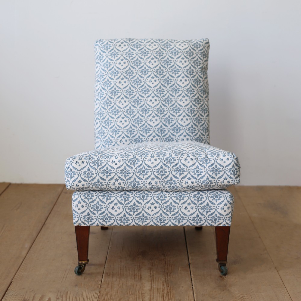 An armless Victorian slipper chair upholstered in blue and white geometric floral patterned fabric with short mahogany legs on brass castors.