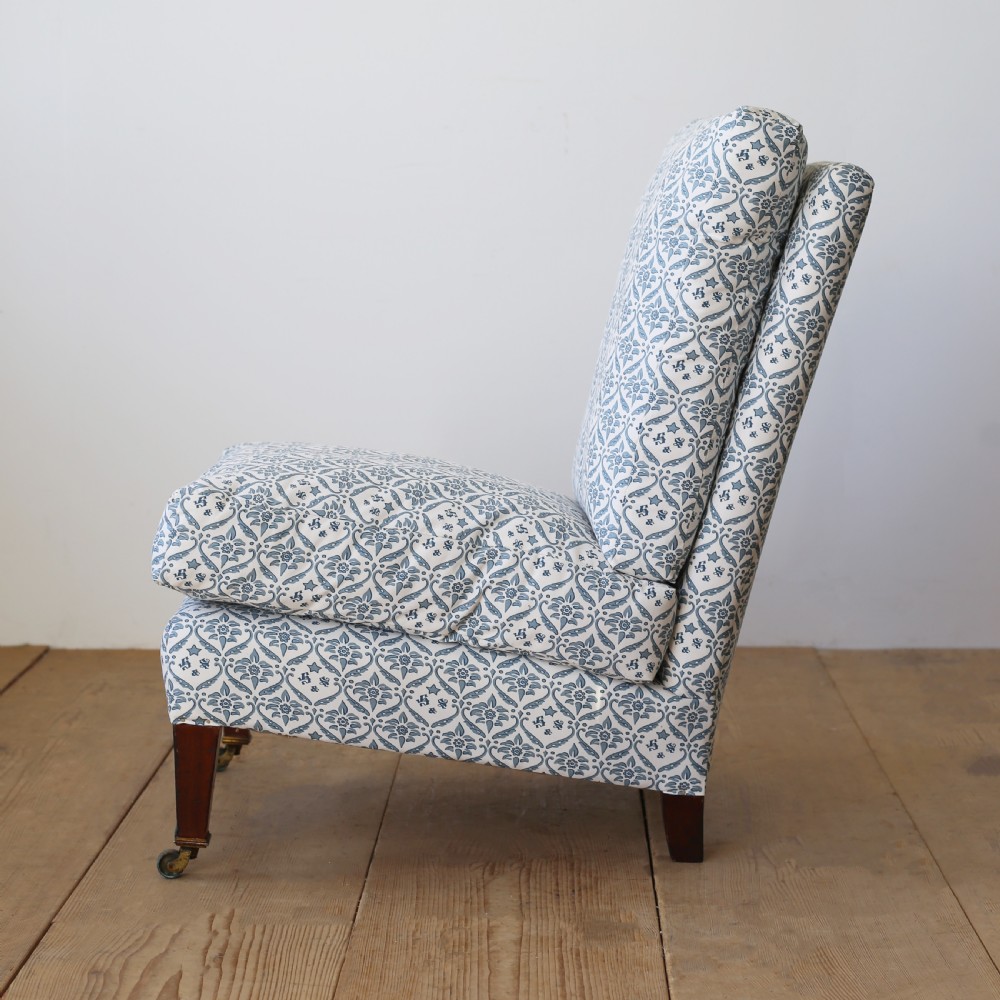An armless Victorian slipper chair upholstered in blue and white geometric floral patterned fabric with short mahogany legs on brass castors. View III