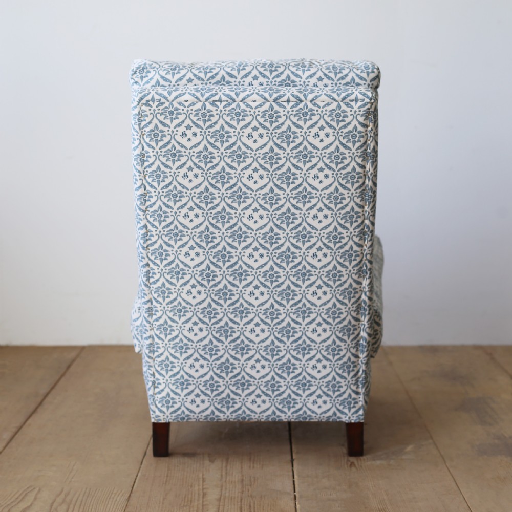 An armless Victorian slipper chair upholstered in blue and white geometric floral patterned fabric with short mahogany legs on brass castors. View IV