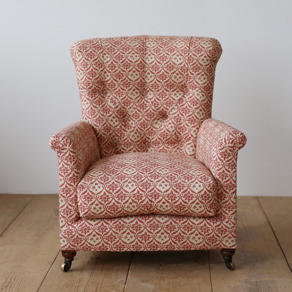 A nineteenth-century Victorian Howard and Sons armchair upholstered in red and cream patterned fabric with a button-backed tufted backrest, deep cushion seat, and turned front legs on brass castors.