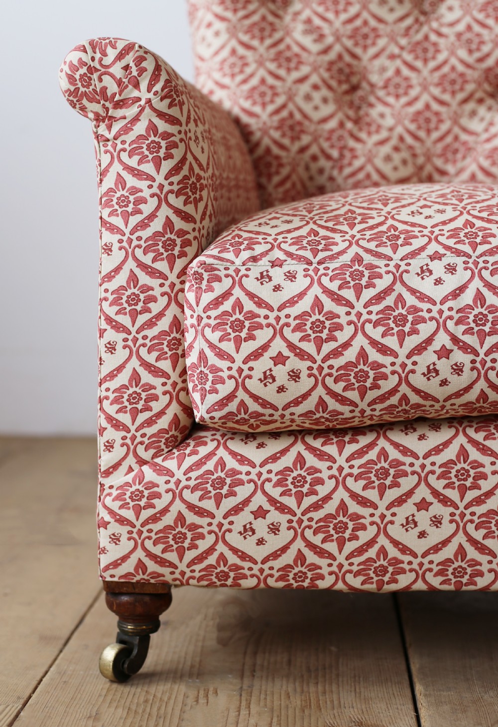 A nineteenth-century Victorian Howard and Sons armchair upholstered in red and cream patterned fabric with a button-backed tufted backrest, deep cushion seat, and turned front legs on brass castors. View II