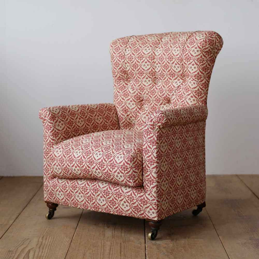 A nineteenth-century Victorian Howard and Sons armchair upholstered in red and cream patterned fabric with a button-backed tufted backrest, deep cushion seat, and turned front legs on brass castors. View III